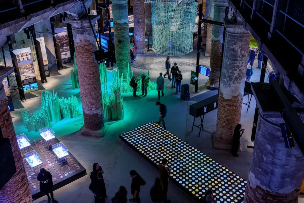 Interno dell’Arsenale – Installazioni sofisticate tra pilastri e display luminosi, in uno spazio che invita all’esplorazione dei progetti espositivi